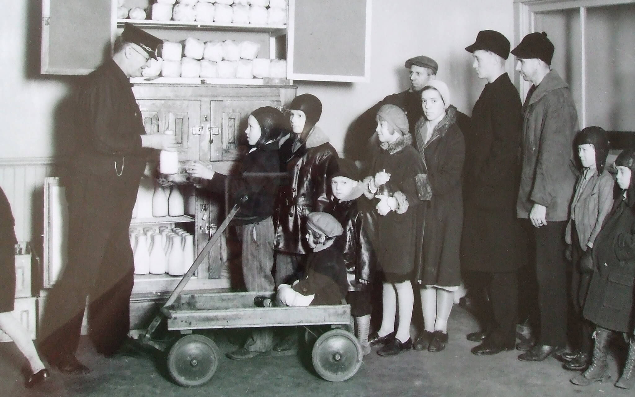 Vintage photo of children lining up to receive bottles of milk during the great depression